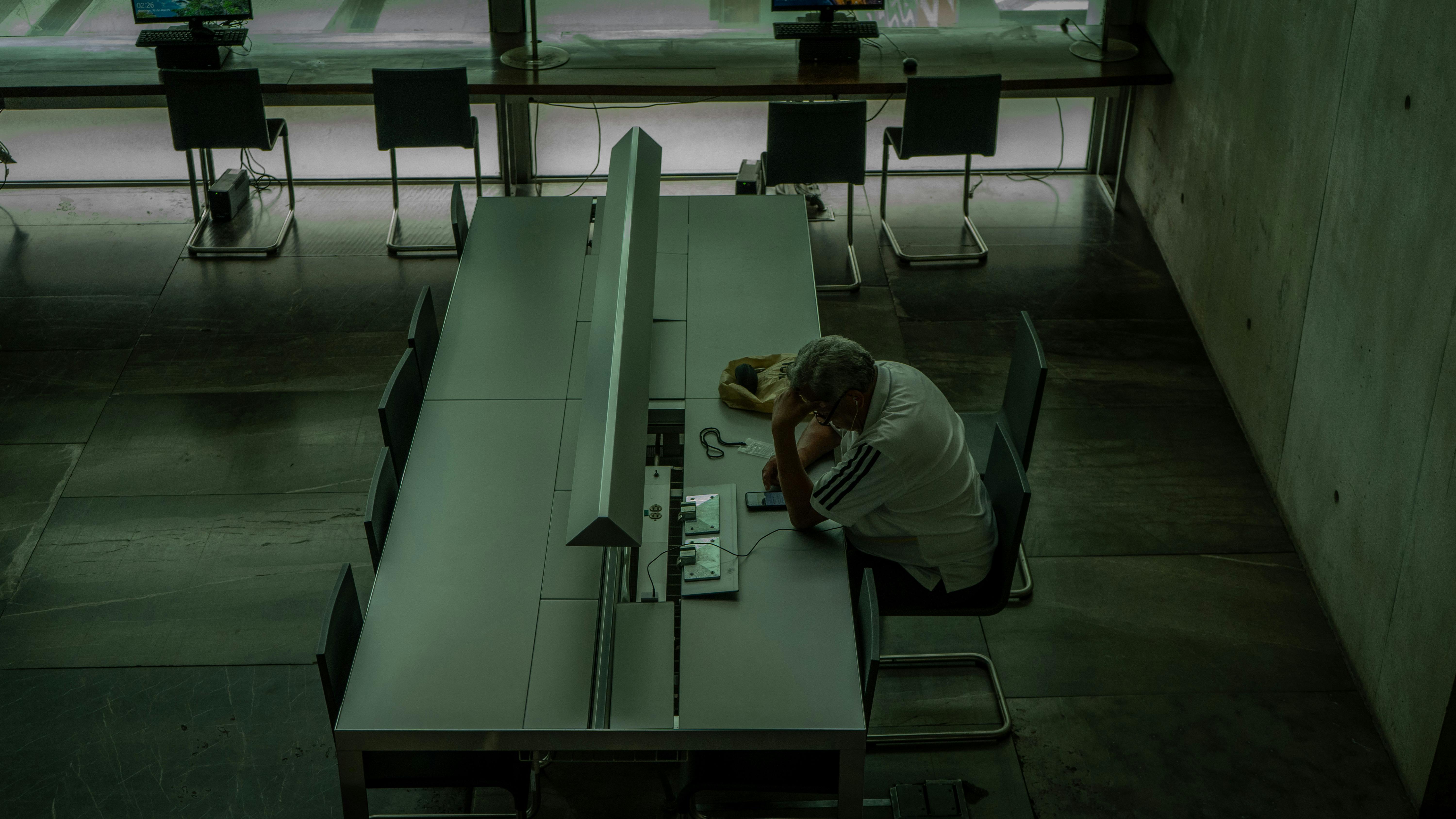 Man Sitting by a Desk and Bending over his Phone · Free Stock Photo