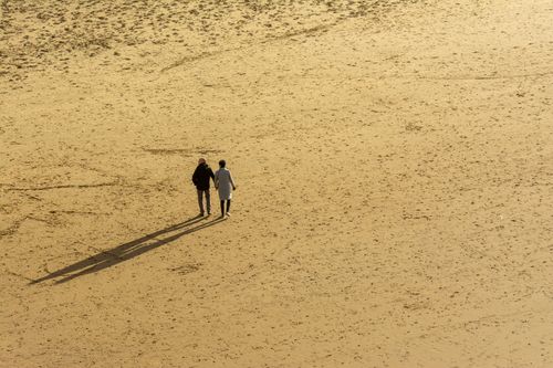 Free A couple walking hand in hand across a vast sandy landscape, casting long shadows. Stock Photo