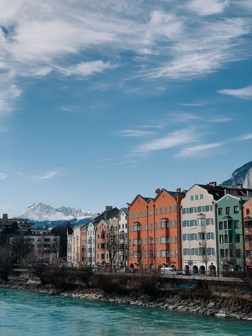 Free Vibrant buildings line the Inn River in Innsbruck, framed by mountains and a clear blue sky. Stock Photo
