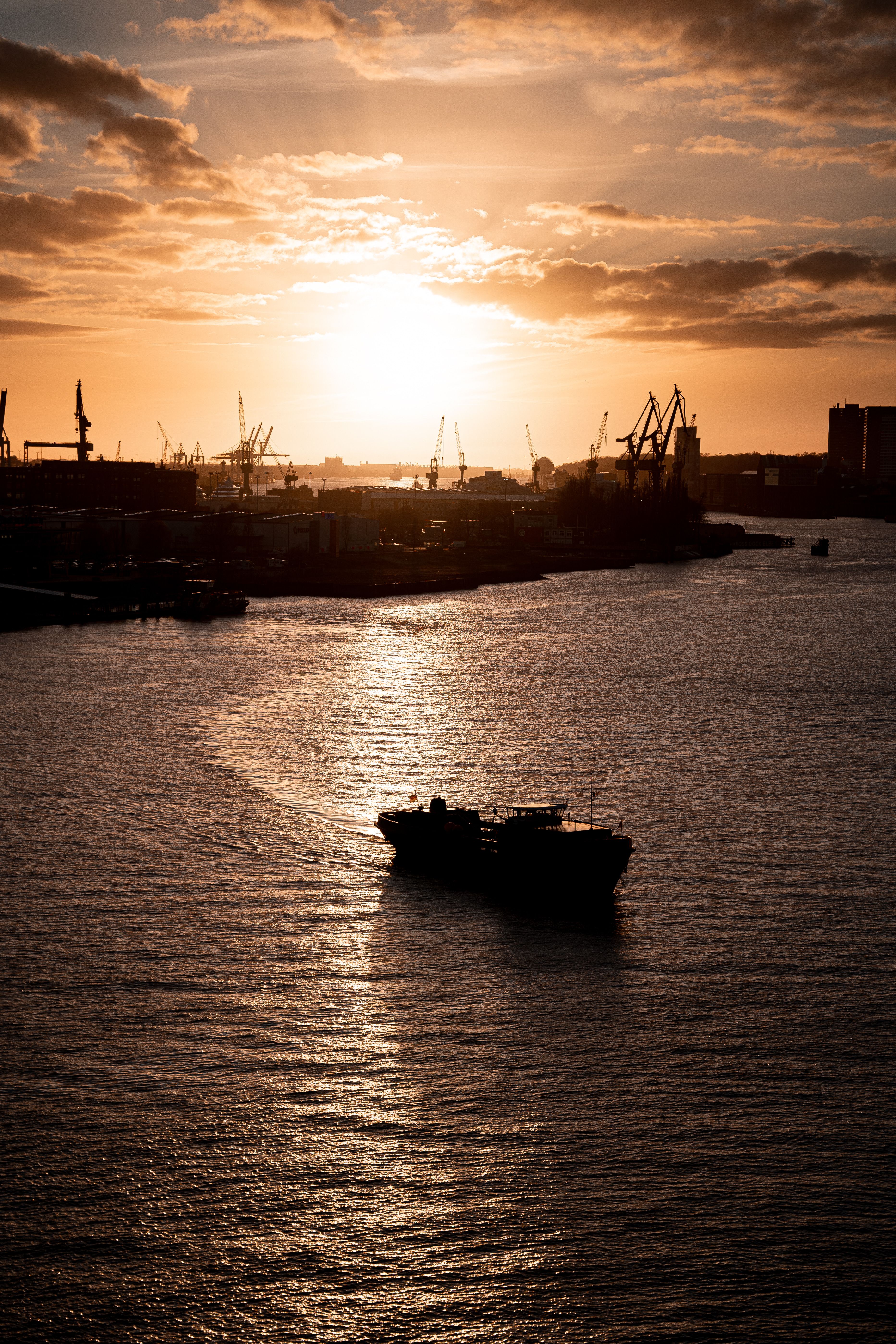 Silhouette of a cargo ship against a sunset in Hamburg harbor. Tranquil and industrial scene.