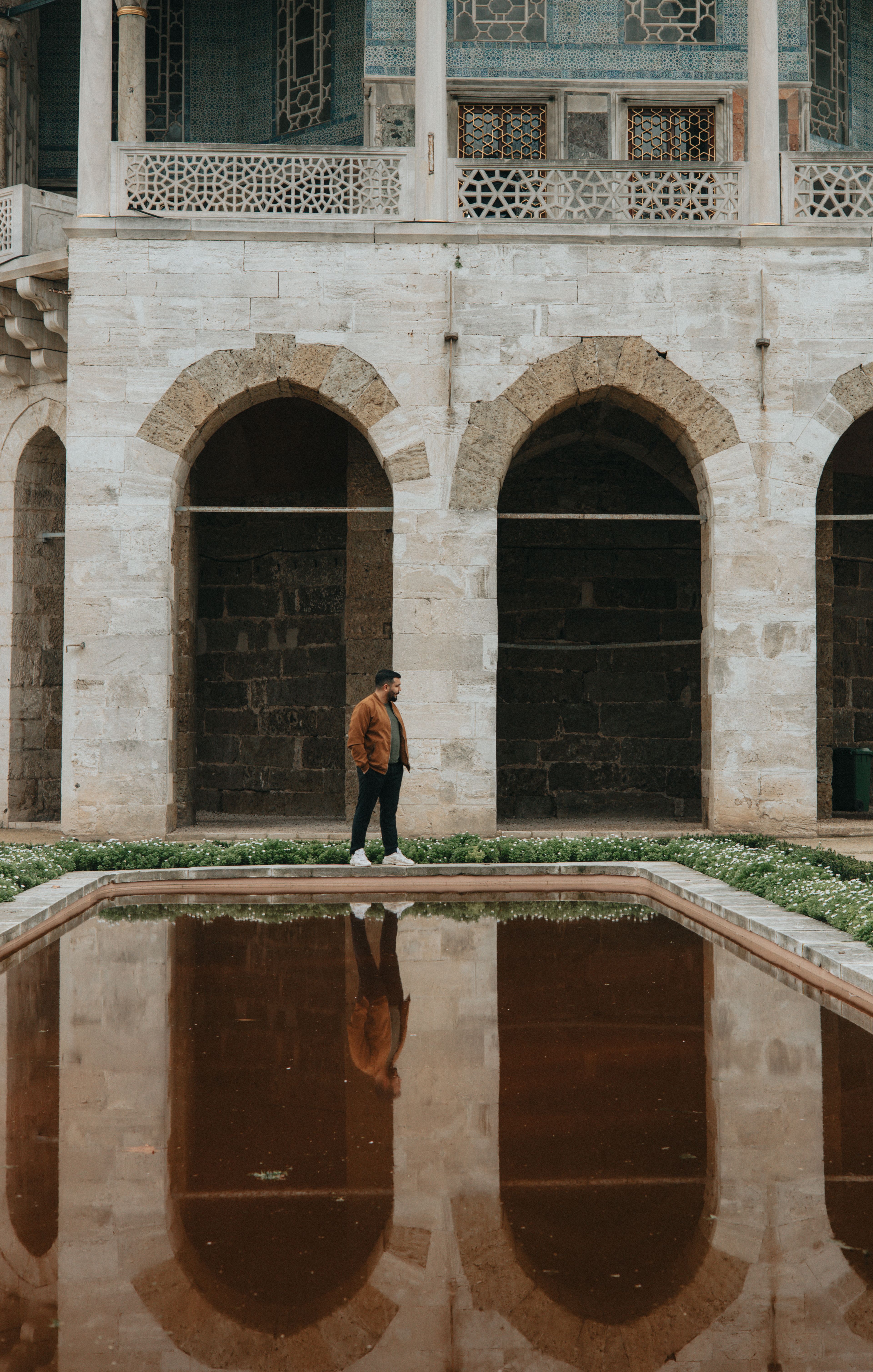 A man stands by a reflective pond at Topkapi Palace, showcasing its historic architecture.