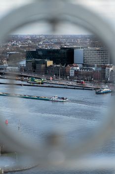 Dynamic cityscape view featuring river, barges, and modern buildings through a circular frame. — photo by Wolf  Art