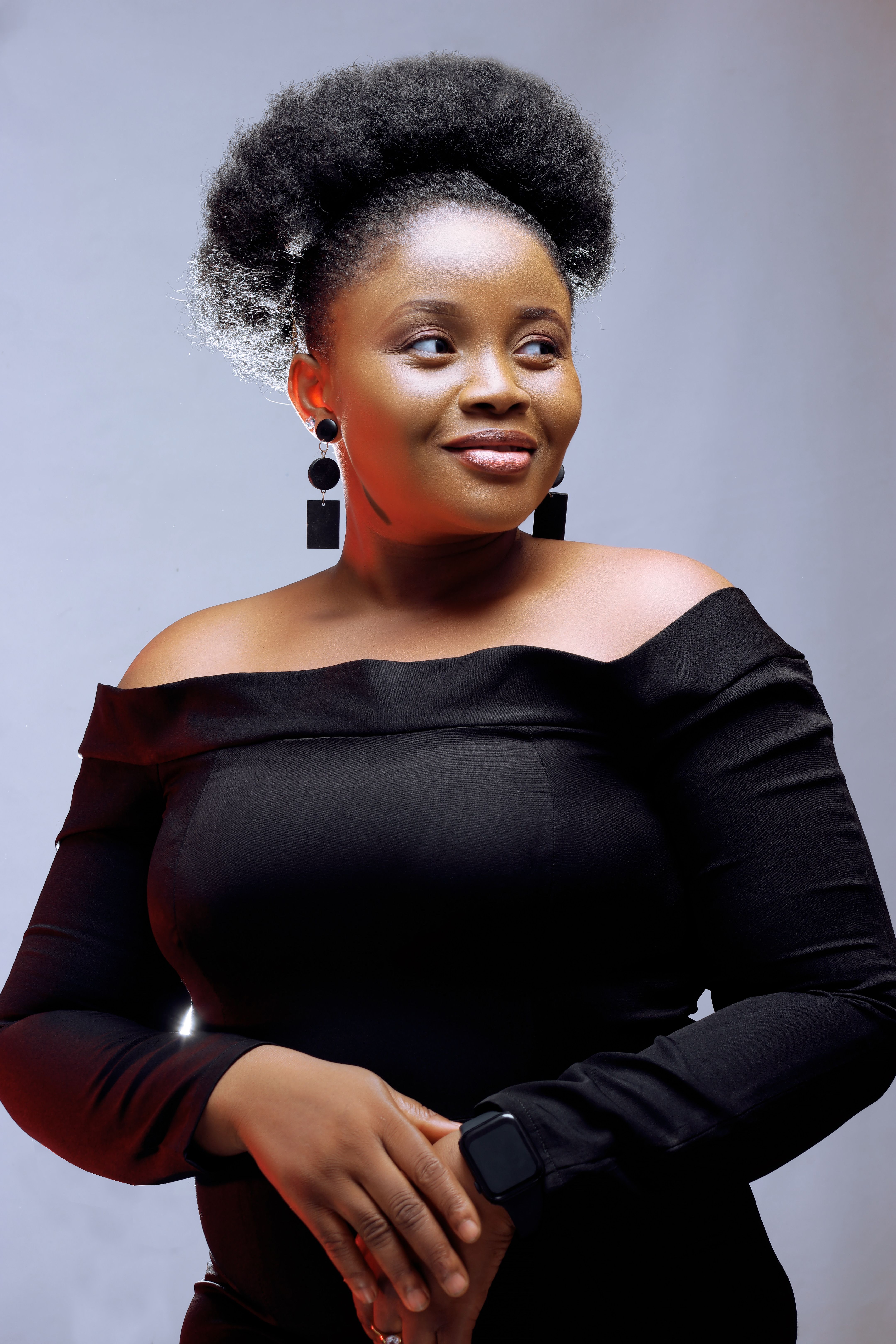 Portrait of a stylish African American woman with an afro hairstyle, wearing a black top and earrings. Studio setting.