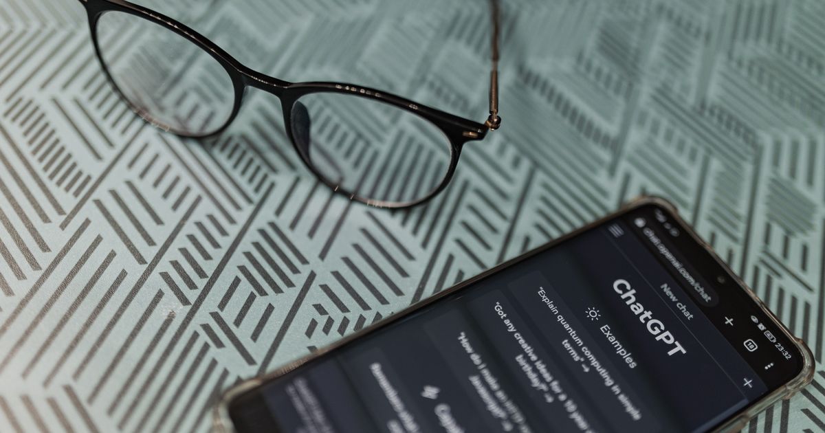 Eyeglasses resting beside a smartphone that shows the ChatGPT app on a patterned surface