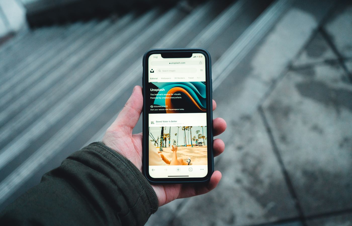 A person holds a smartphone while browsing a webpage outdoors. Urban setting.