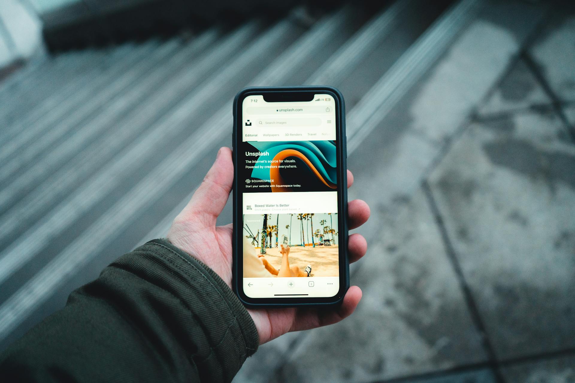 A person holds a smartphone while browsing a webpage outdoors. Urban setting.