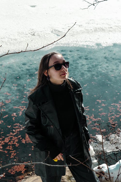 Young Woman Wearing a Black Coat Standing at the Edge of a Pond in Winter