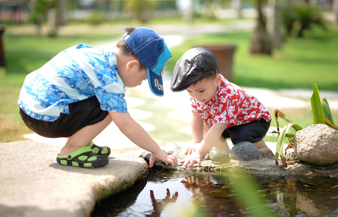 Boy in Blue and White Shirt Playing Near on Body of Water With Boy in Red Shirt