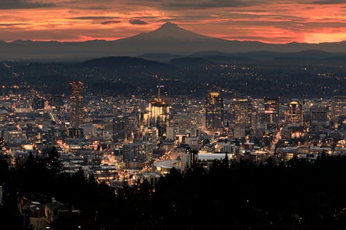 Free View of Illuminated Buildings in Portland and Mountains in the Background at Sunset Stock Photo