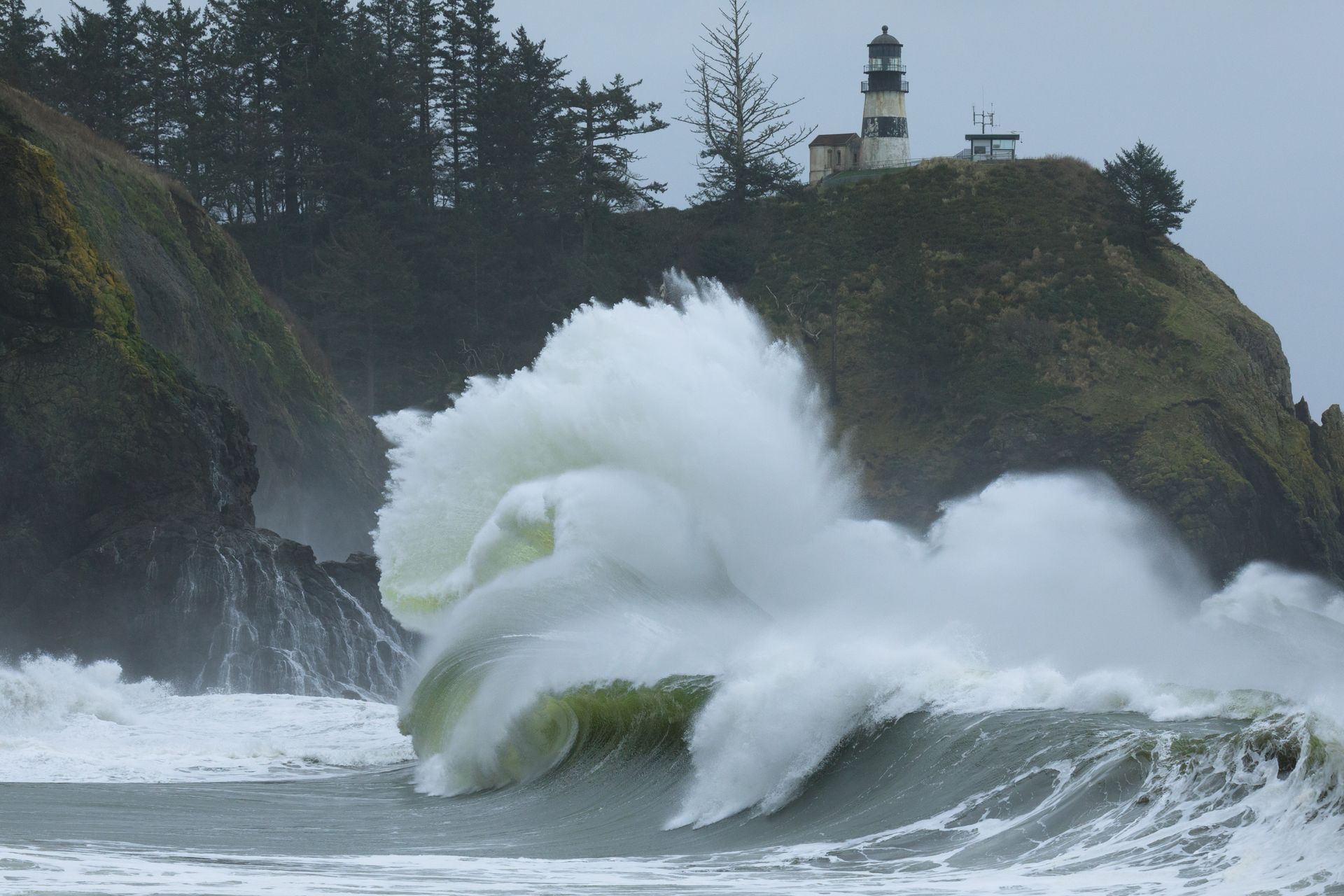 Powerful waves crash against cliffs beneath a lighthouse, showcasing nature's raw energy by the sea.