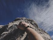 在晴朗的蓝天下，一名登山者的手紧紧抓住岩石悬崖，展现出冒险精神