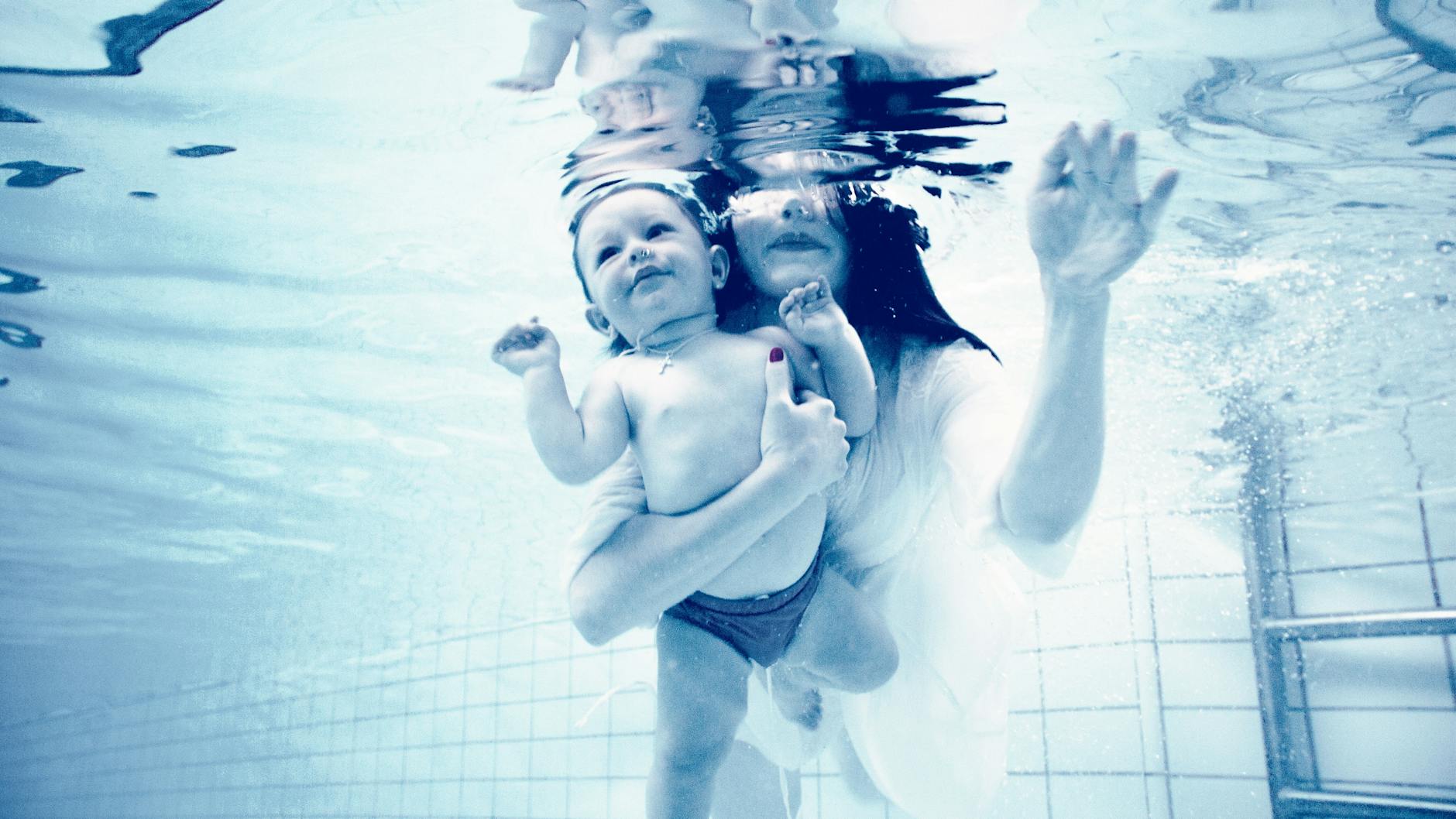 grayscale photography of woman holding baby in swimming pool