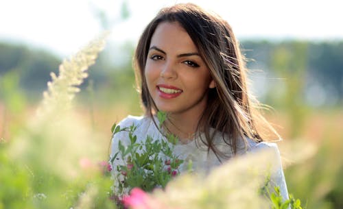 Free Woman in White Crew Neck Shirt Smiling and Surround With Flowers and Plants during Daytime Stock Photo