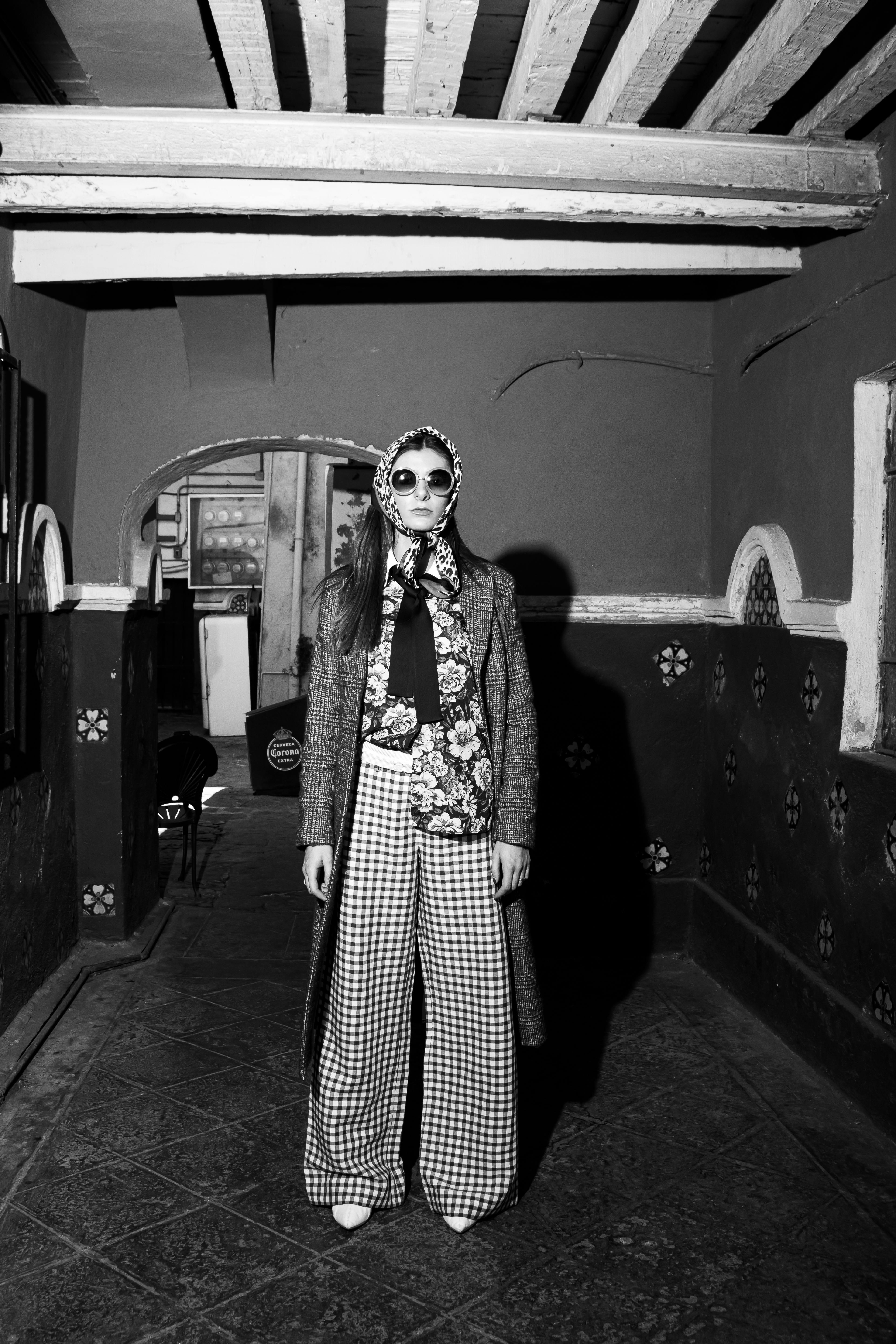 Monochrome portrait of a stylish woman in vintage attire with checked pants and floral prints.