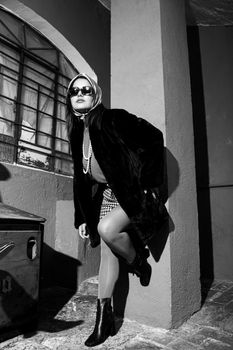 Stylish woman in a vintage black outfit with headscarf poses outdoors.