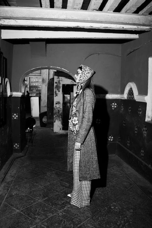 Young Woman Wearing a Headscarf and an Overcoat Standing in the Middle of a Room