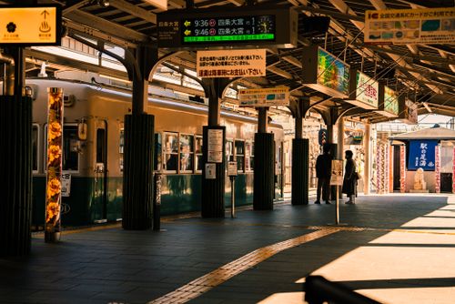 Free People waiting at a sunlit urban train station platform with vintage-style train and signage. Stock Photo