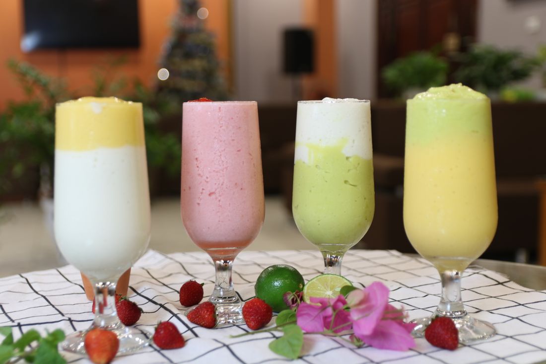Four layered smoothies in stemmed glasses with strawberries, limes and pink flowers on a checked cloth