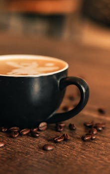 A warm close-up view of a coffee cup surrounded by roasted beans on a wooden surface.