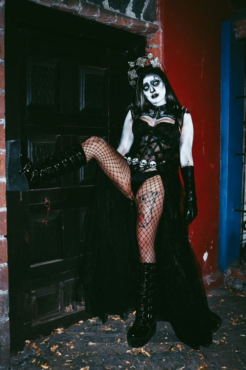 Free A woman in gothic Halloween costume poses against a dark door, exuding eerie vibes. Stock Photo