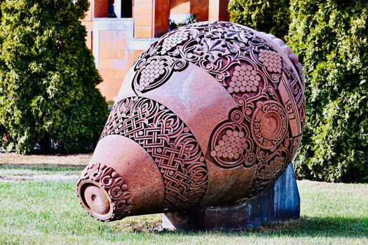 Ornate ceramic sculpture with detailed carvings displayed in an outdoor park setting.