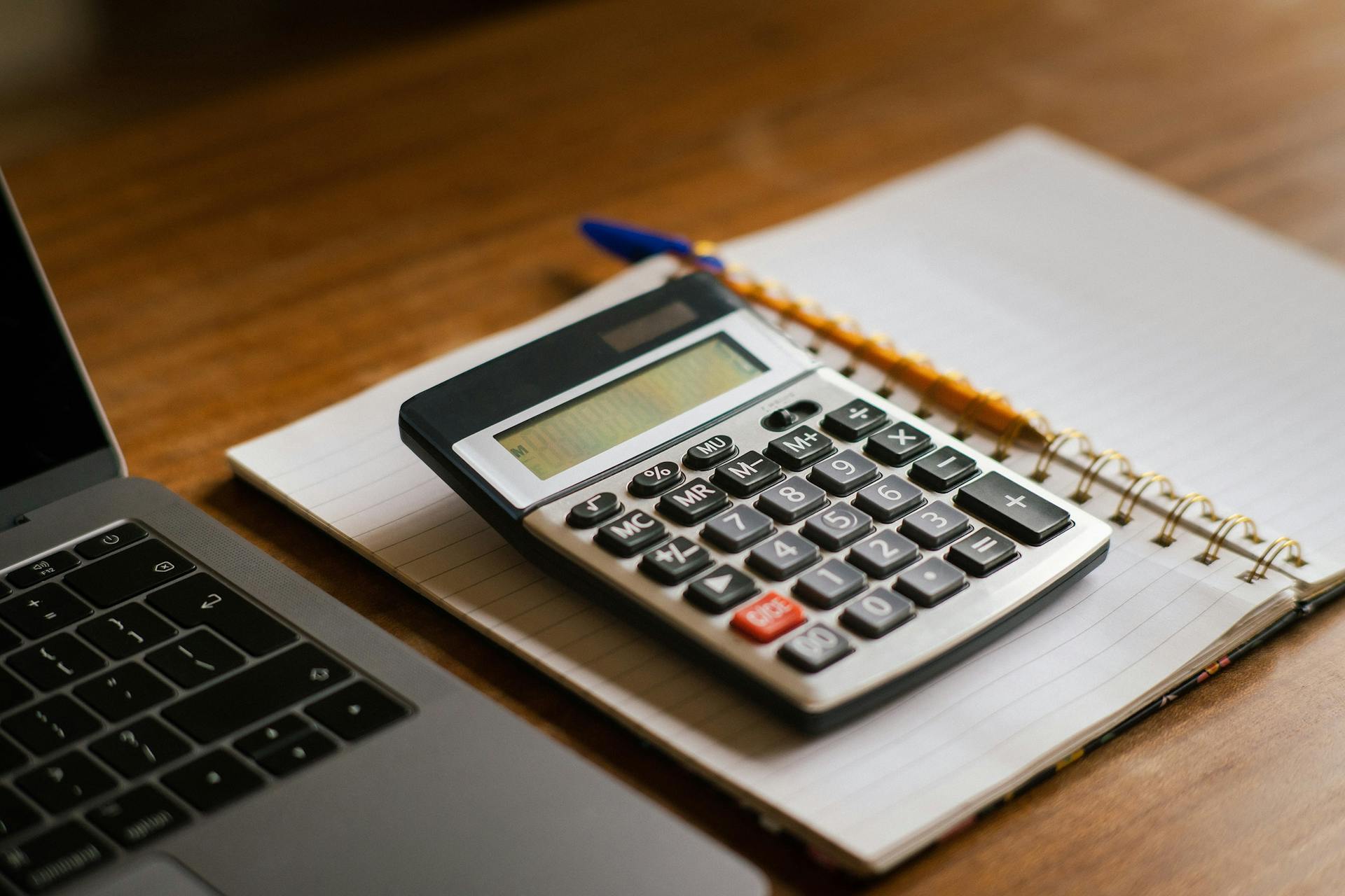 Calculator and open laptop on wooden desk, ideal for financial or accounting tasks.