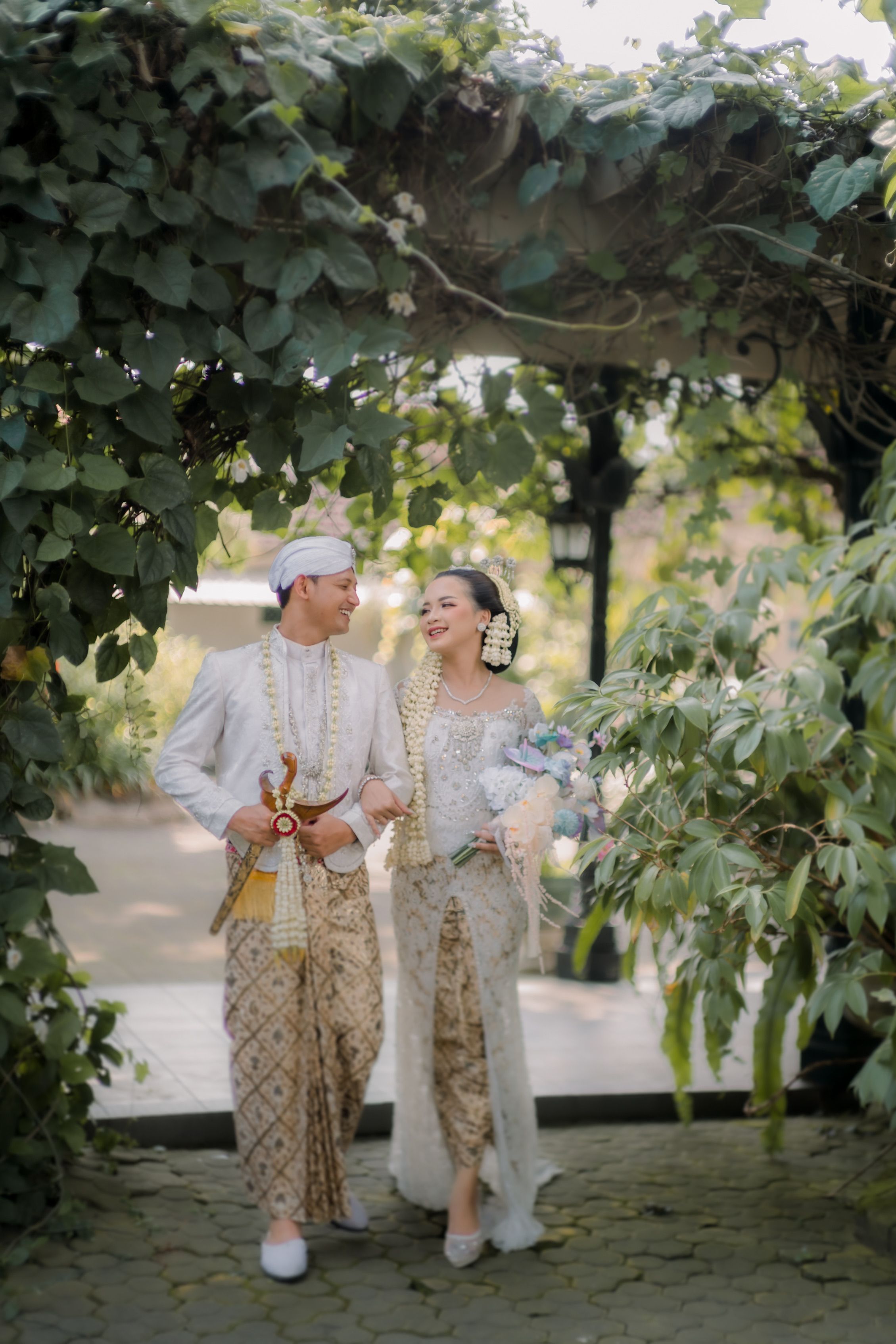 Joyful couple in traditional attire in a lush garden setting.