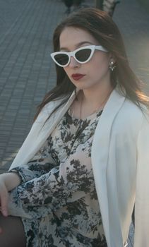 Elegant young woman in sunglasses and floral dress posing confidently outdoors