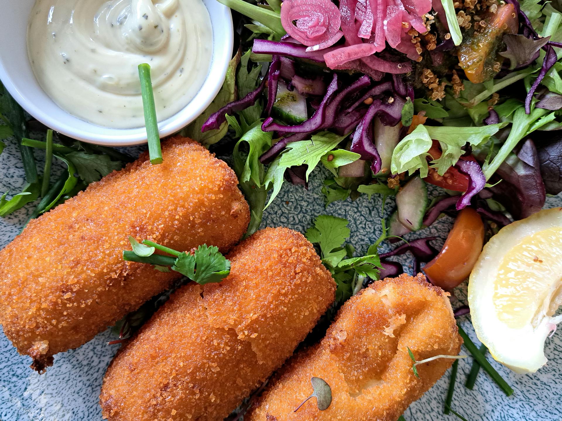 Enjoy crispy fish croquettes paired with a vibrant salad and tangy sauce.