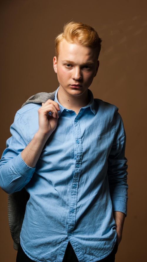 Free Portrait of a young redhead man in a blue shirt posing confidently in a studio setting. Stock Photo