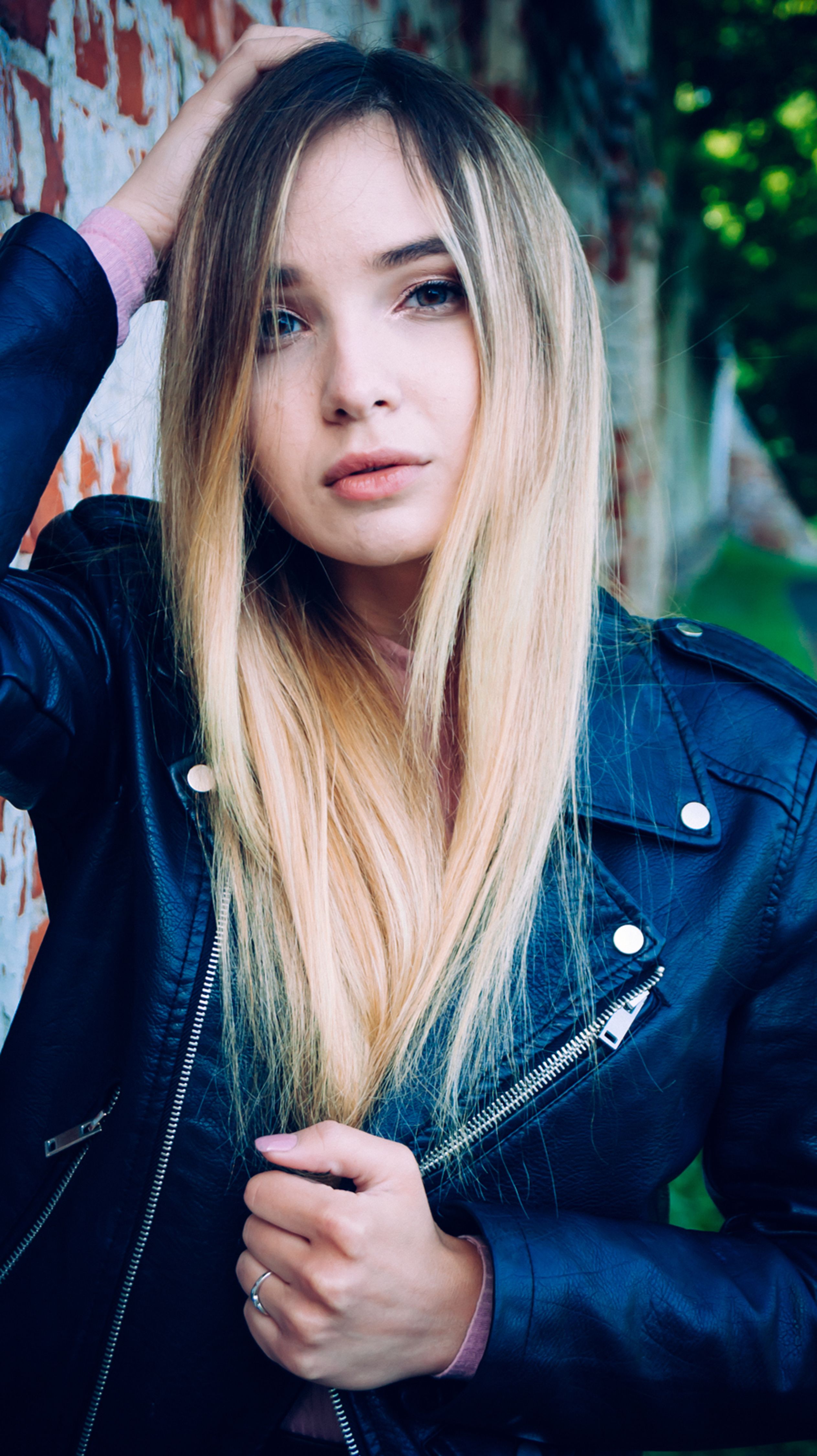 Portrait of a young woman in a leather jacket against a brick wall, evoking rebellious fashion vibes.