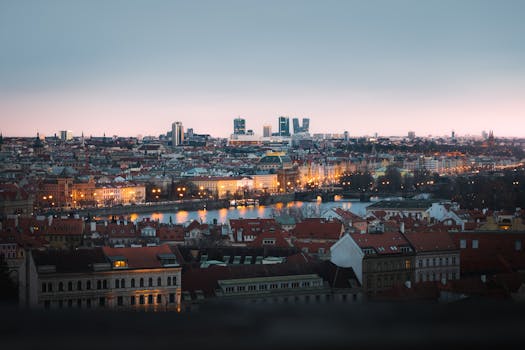 Panoramic view of Prague cityscape at dusk, highlighting Vltava river and historical buildings.