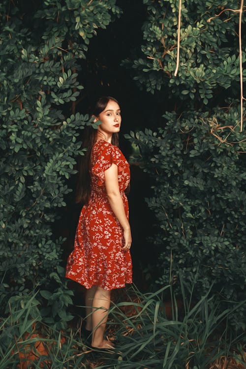 Beautiful Brunette Woman in Red Dress Standing Among Leaves