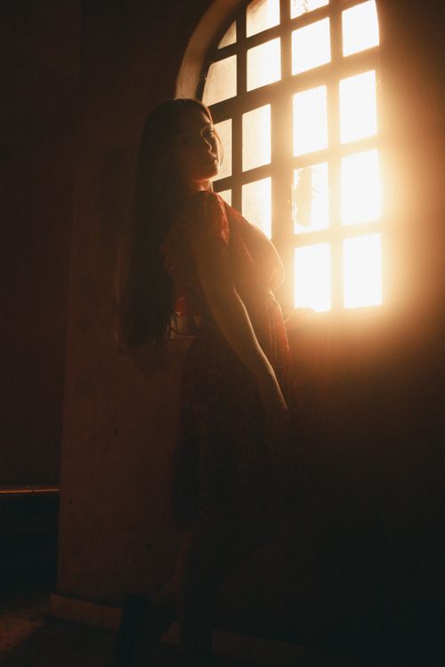 Free Artistic silhouette of a woman standing by a window, captured in warm sunlight. Stock Photo