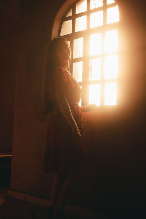 Free Silhouette of a woman standing by a sunlit window, creating a mystical atmosphere indoors. Stock Photo