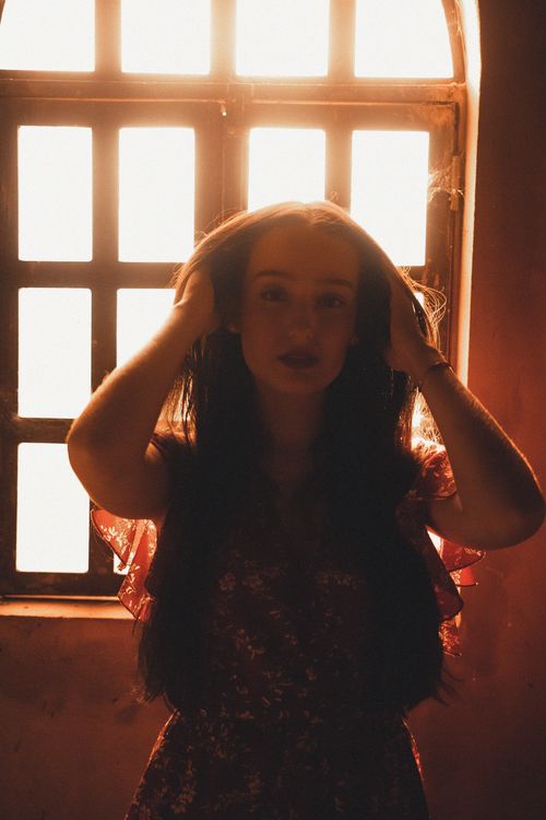 Free Dramatic silhouette of a woman with long hair standing by a glowing window. Stock Photo