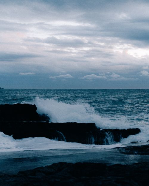 Free Serene evening view of ocean waves crashing onto rocks beneath a cloudy sky. Stock Photo