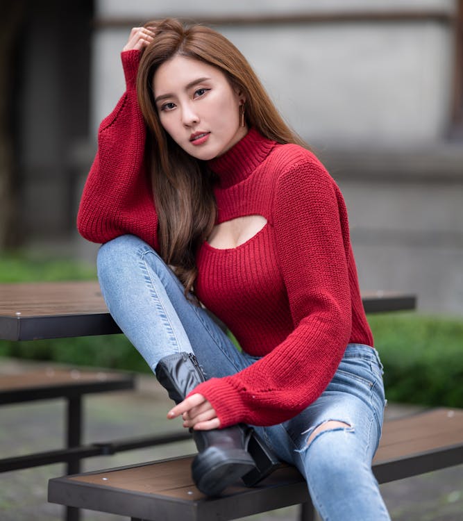 Young Woman in a Red Sweater and Jeans Sitting on a Bench 