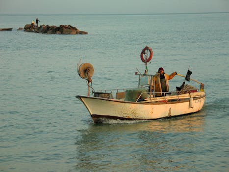 A fisherman navigates a rustic boat on tranquil waters near the rocky shoreline.