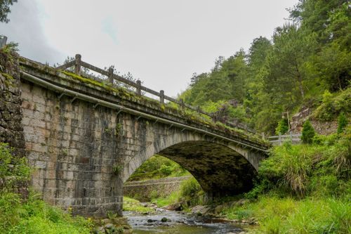 Free A scenic stone bridge over a tranquil river surrounded by lush greenery. Stock Photo