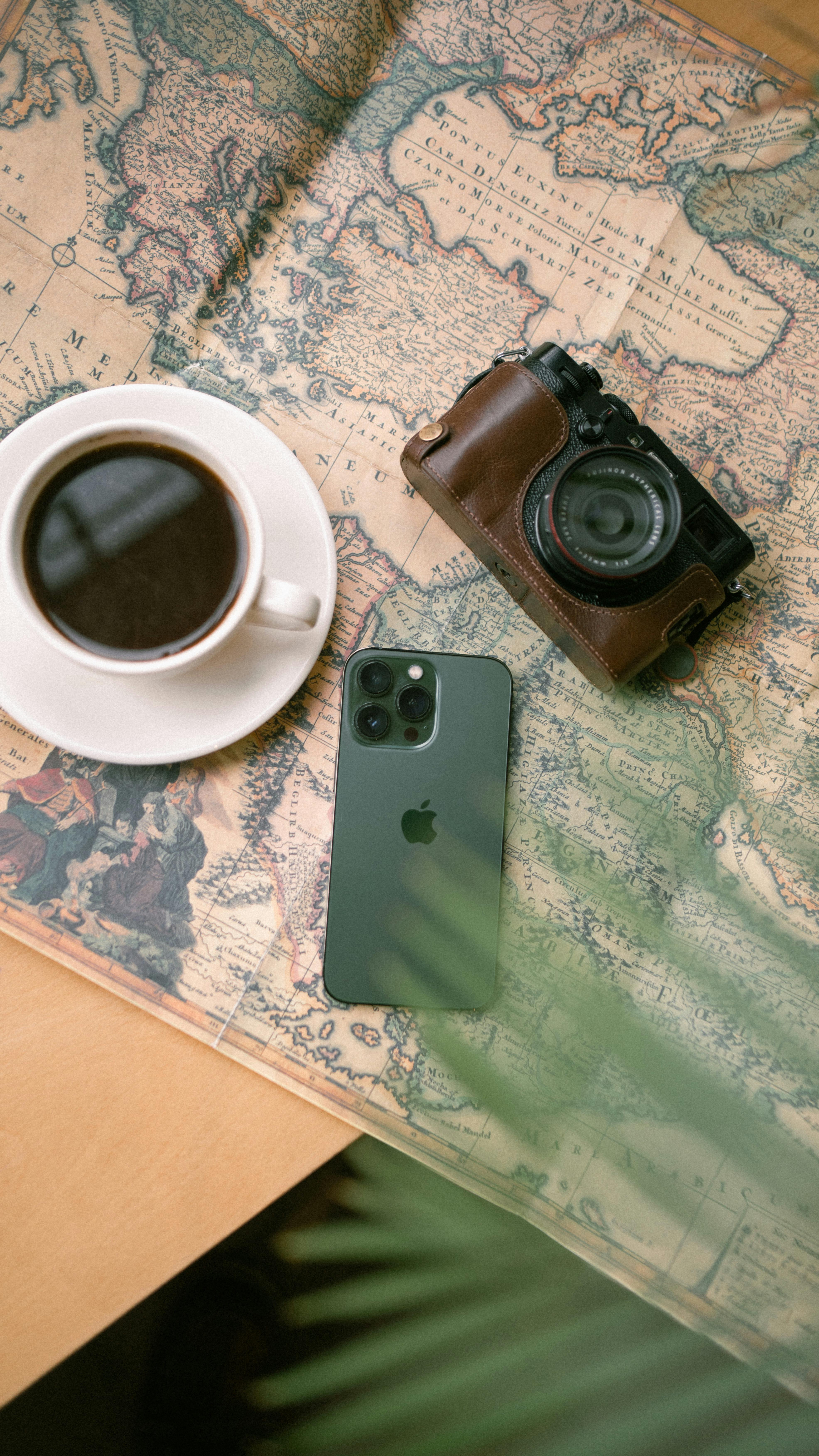 Top-down view of a coffee cup, vintage camera, and smartphone on a world map.