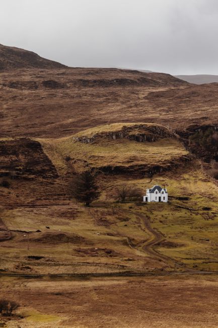 A serene view of a solitary cottage nestled in the rugged landscape of the Scottish Highlands.