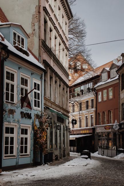 Snow-covered street in Old Town Riga with colorful historic buildings and cozy cafes.