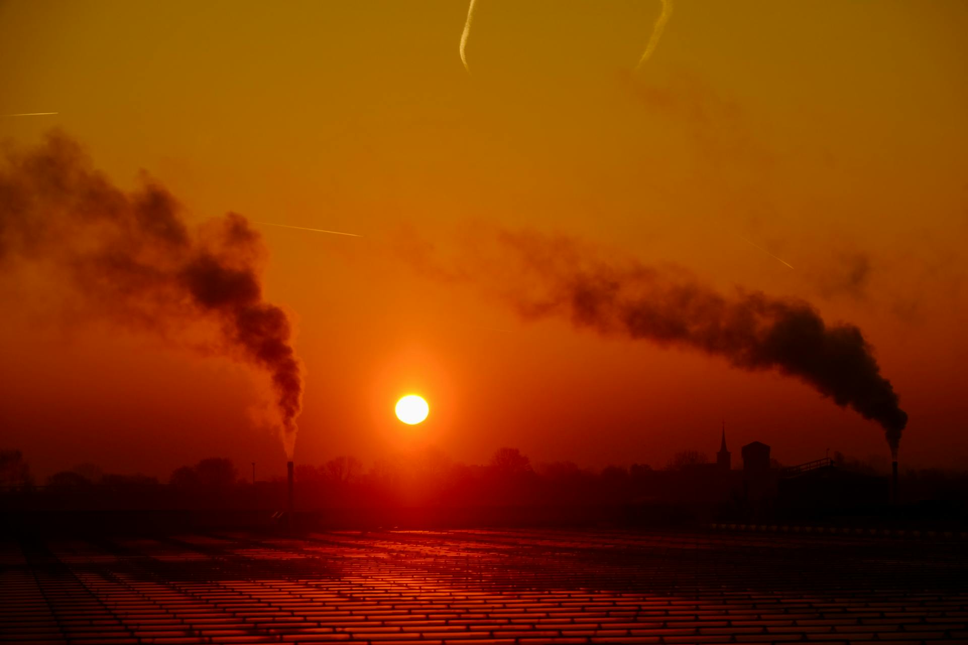 Sunset over an industrial landscape with smoke emissions highlighting air pollution.