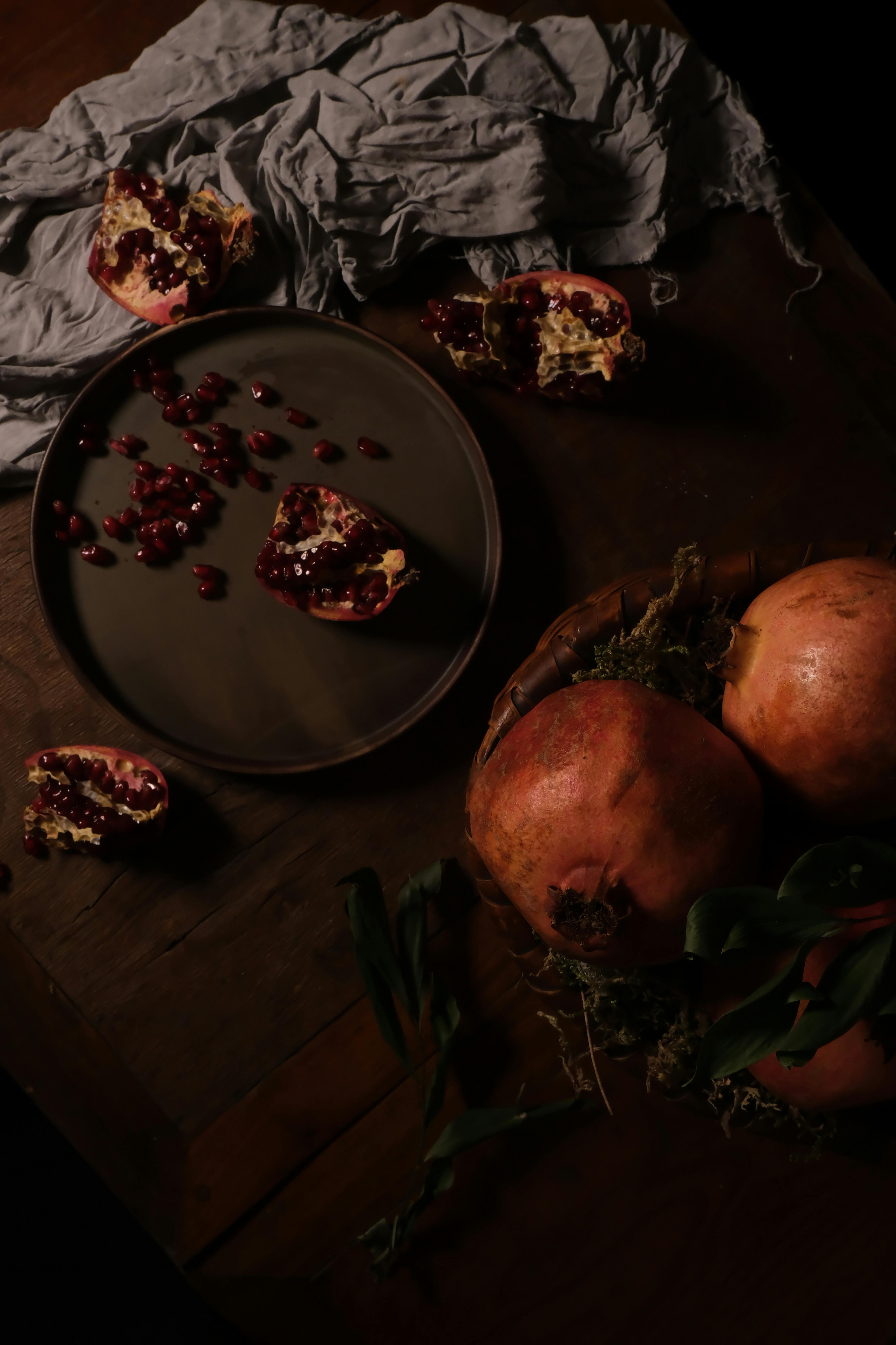 Moody still life of pomegranates and seeds on a dark wooden table with artistic composition.