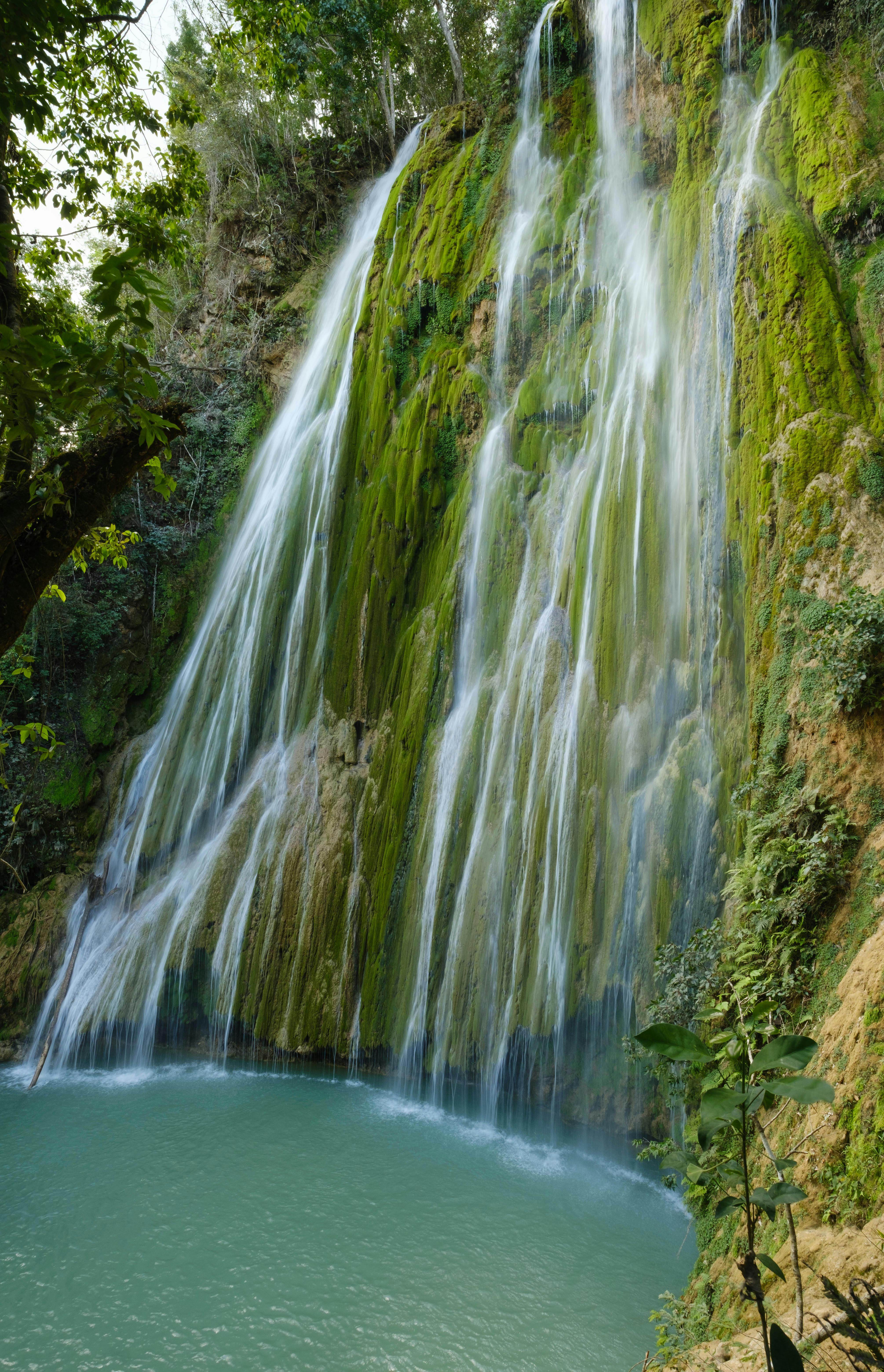 A tranquil waterfall flows over lush green moss-covered rocks into a turquoise pool.