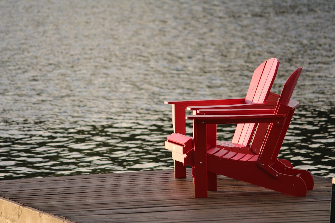 Roter Hölzerner Lounge Chair Auf Brown Boardwalk In Der Nähe Von Gewässern Während Des Tages