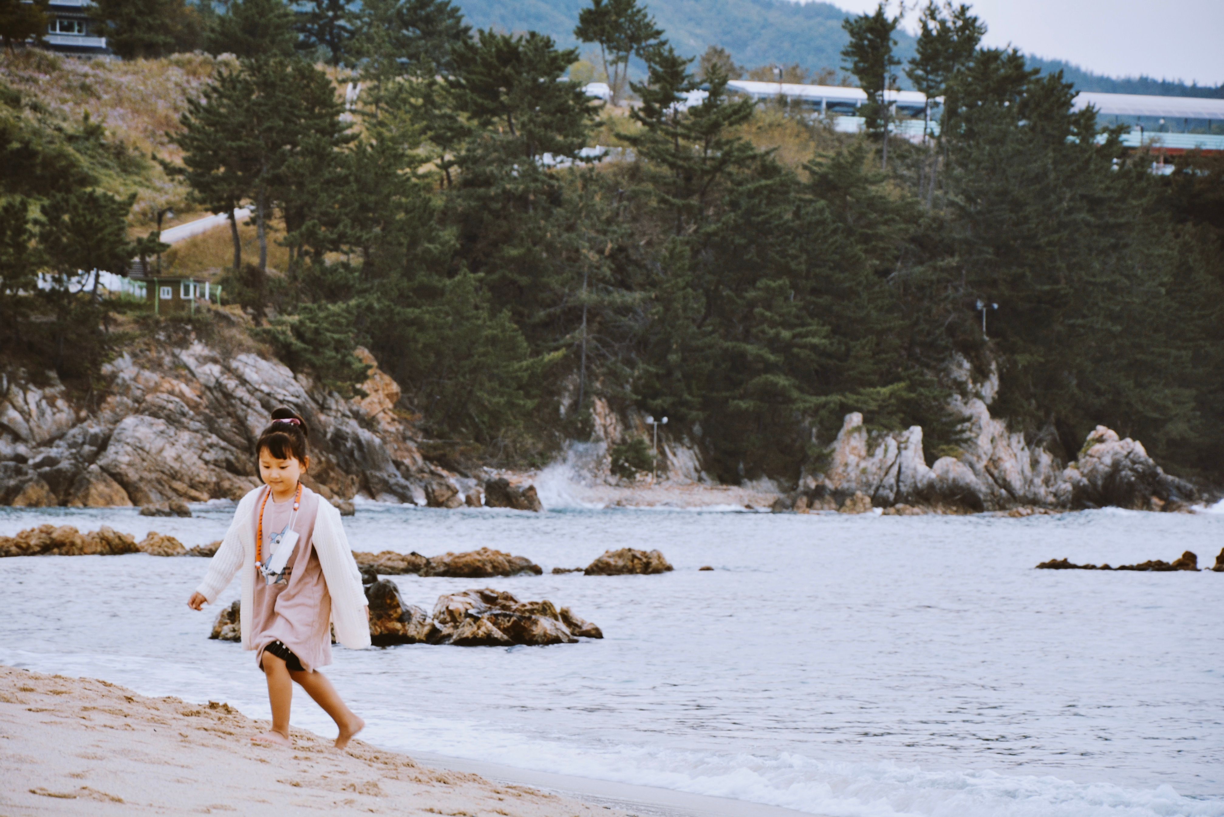 A young girl walks along a scenic South Korean beach, surrounded by nature and the ocean.