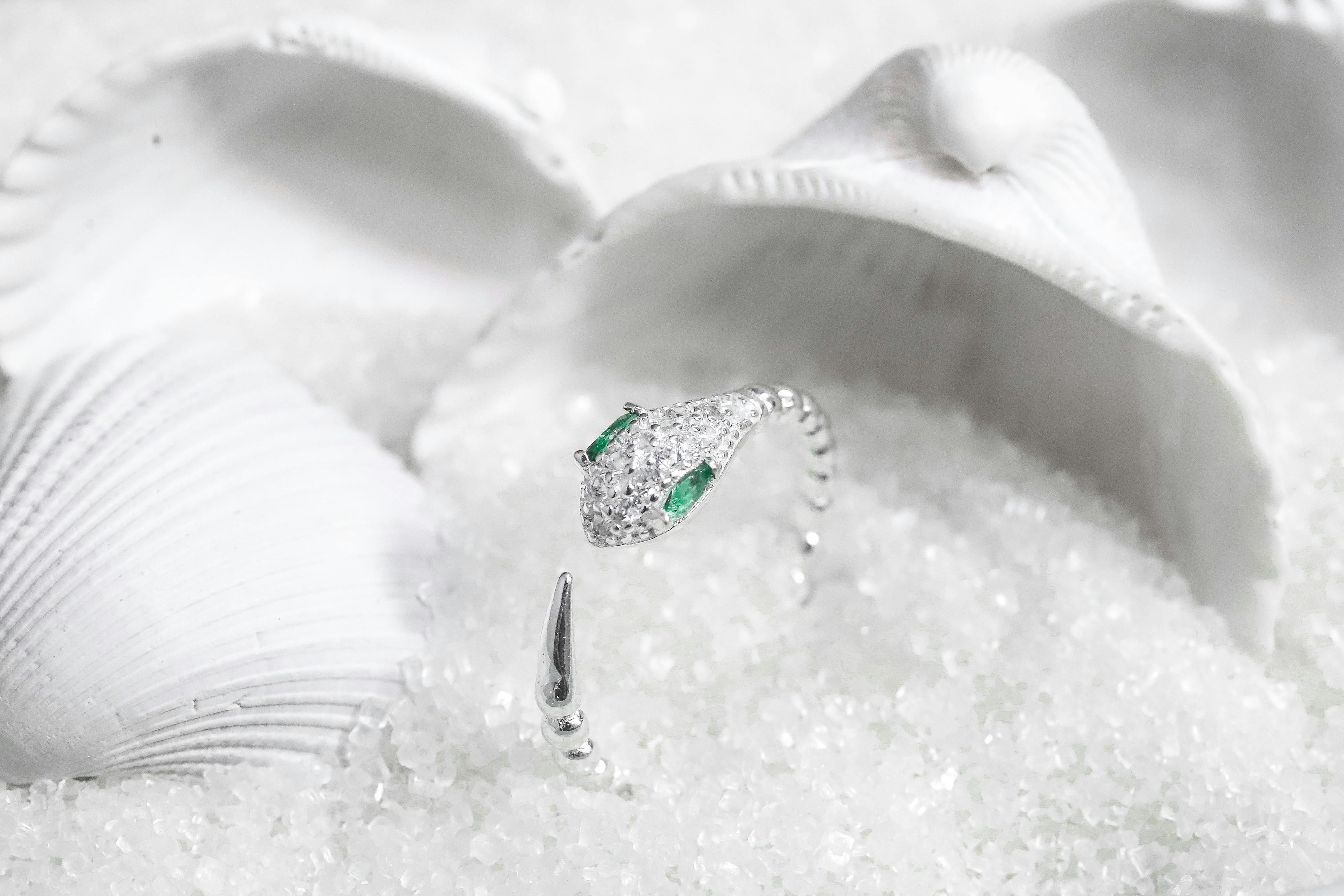 Luxurious diamond snake ring with emerald eyes, elegantly displayed among white seashells.