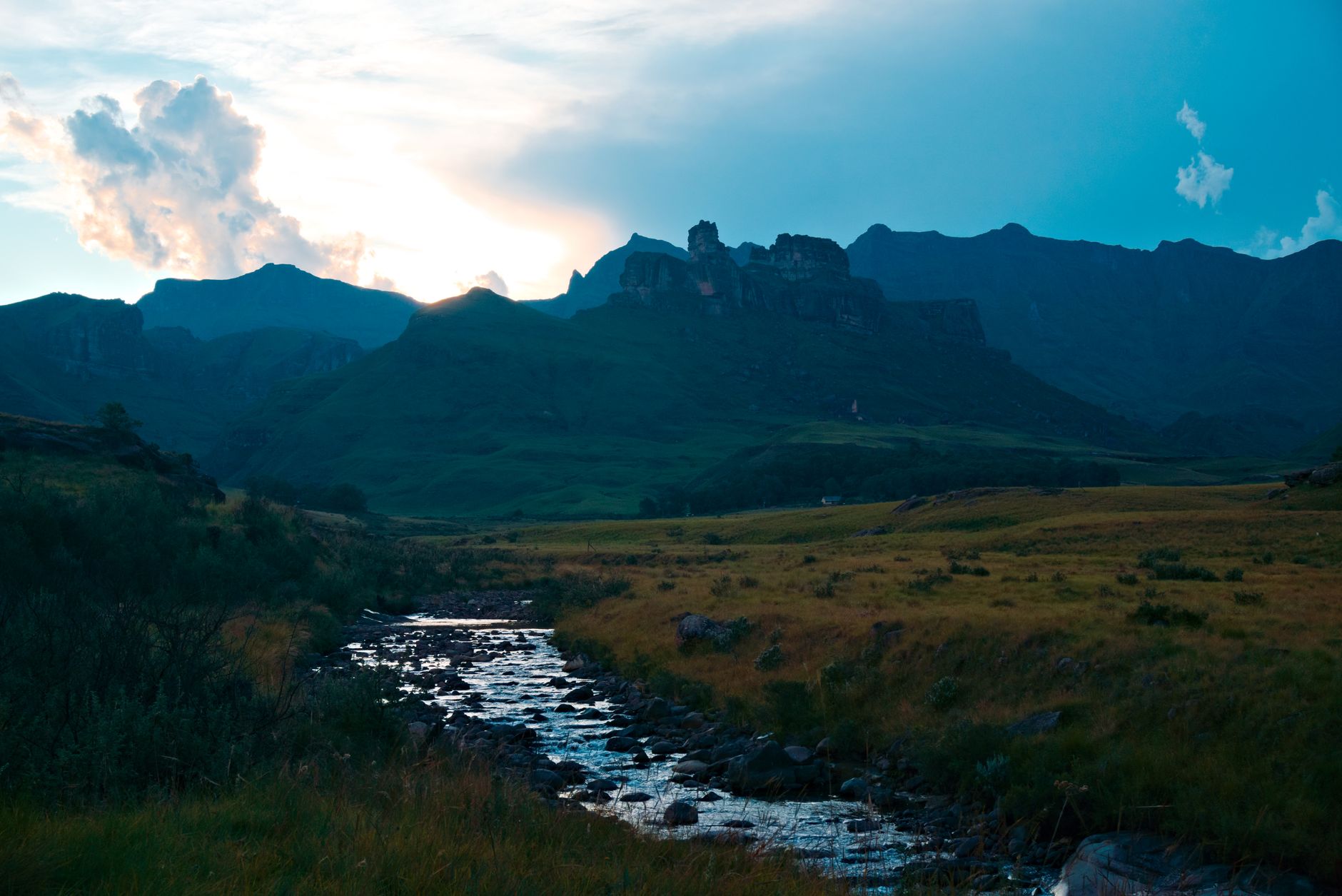 Captivating mountain landscape with a flowing stream and dramatic sky at dawn.